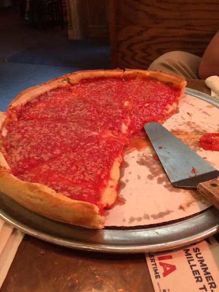 A large pizza with a thin crust, topped with tomato sauce, on a metal tray, with a pizza cutter nearby, served at a restaurant.
