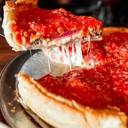 A slice of pepperoni pizza being lifted from a whole pizza with melted cheese stretching.